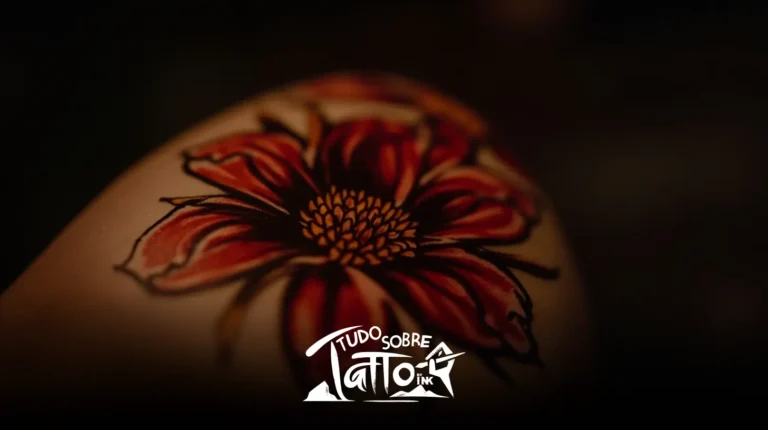 Close de uma tatuagem de flor vermelha e amarela na pele, com o logotipo “Tudo Sobre Tatu Ink” na parte inferior central da imagem.